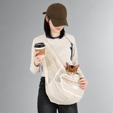 Person carrying a cat in a Milk Brown mesh sling while holding a takeaway cup.