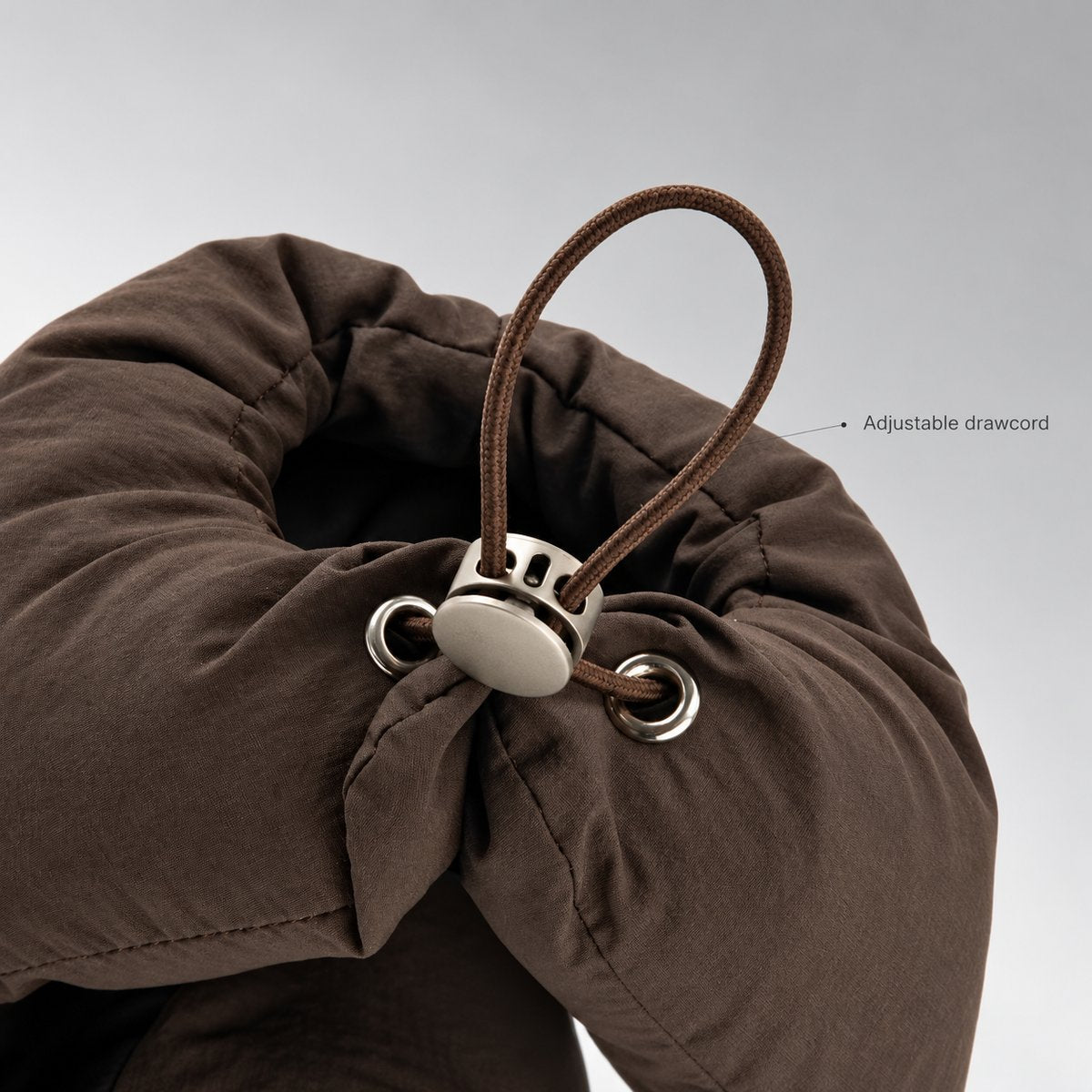 Close-up of the brown hat's drawcord, metal eyelets and round adjustment toggle.