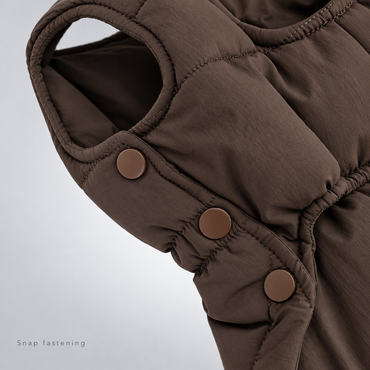 Close-up of the brown snap fastenings beside the vest arm opening and gathered waist.