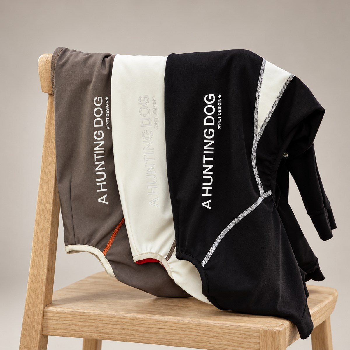 Three sighthound snowsuit colourways draped over a chair, showing the contrasting side panels and back branding.