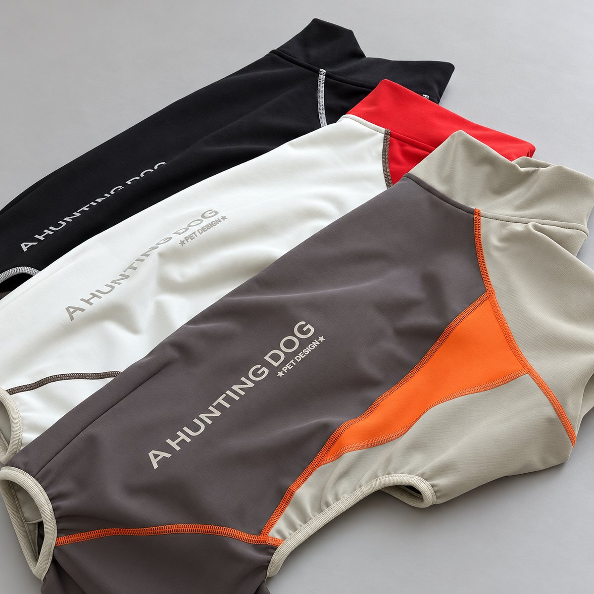 Three colour-block sighthound snowsuits arranged together in slate and orange, ivory and red, and black and ivory.