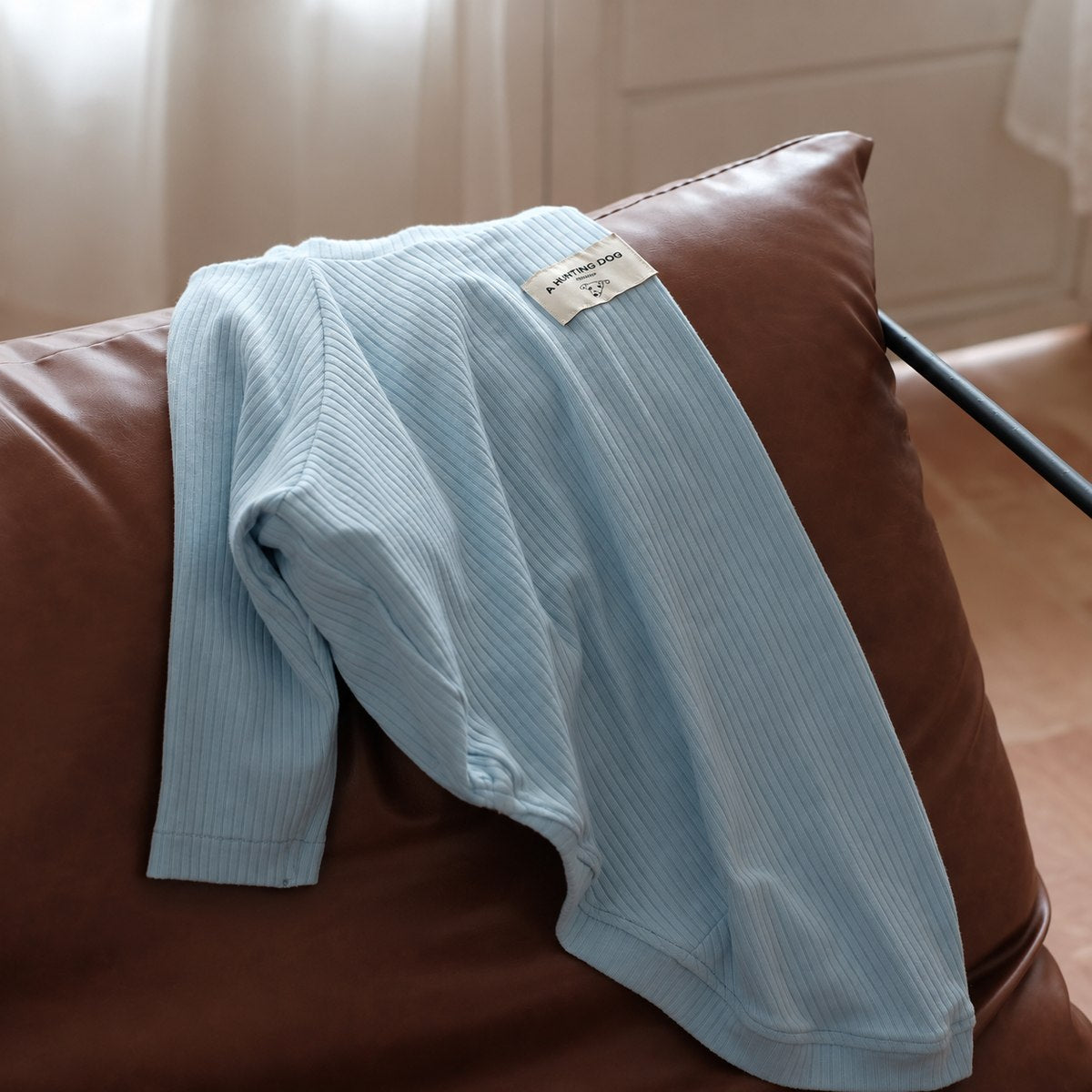 Baby blue ribbed dog turtleneck draped over a leather chair.