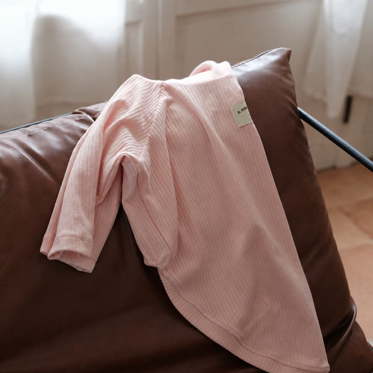 Light pink cotton-blend turtleneck draped over a chair, showing its ribbed fabric and long sleeves.