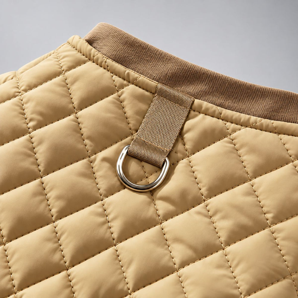 Close-up of the metal back ring and stitched webbing on the tan quilted dog vest.